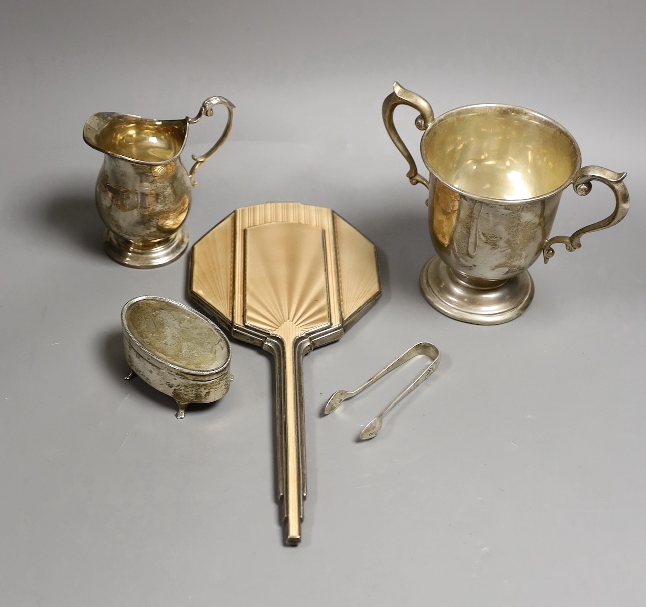 A George V silver two handled pedestal cup, Charles Edwards, London, 1923, height 13.2cm, an Art Deco silver and enamelled hand mirror, Birmingham, 1933, a silver oval trinket box, a silver cream jug and a pair of silver